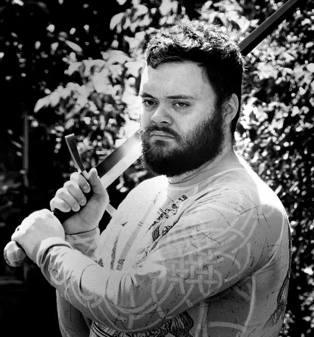 Black and white portrait of Michael Sweeney, owner of Shenandoah Historical Fencing, holding a longsword over his shoulder.